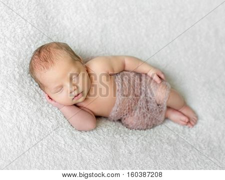 lovely smiling sleeping baby covered with light knitted shawl on white blanket