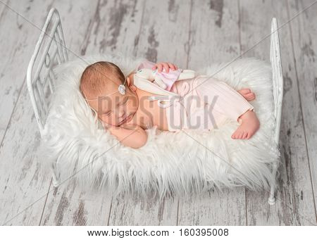 newborn sleeping baby in panties holding toy on cute little bed with white fluffy blanket