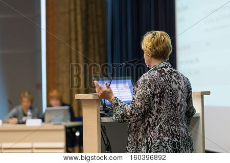Casualy dressed female speaker giving talk at scientific conference. Audience at the conference hall. Business and entrepreneurship event.