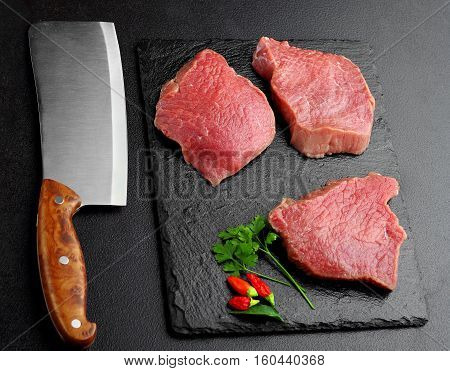Raw Beef Meat With Butcher Knife On Slate Palte With Parsley And Chili Dark Bakcground.selective Foc