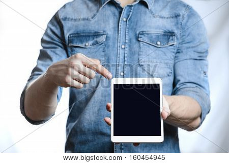 Casual man in denim shirt showing digital tablet computer screen in hands. Isolated on white. Clipping path for display included. He points a finger at the display.