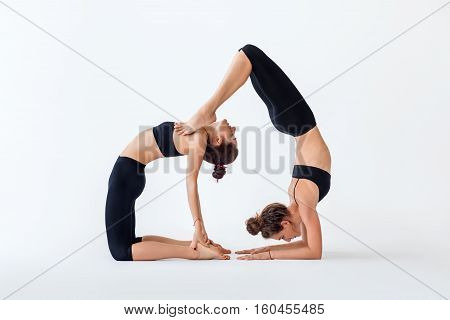 Two Young Women Doing Partner Yoga Asana Camel Pose And Scorpion