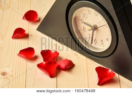 Clock with red rose on wood background.