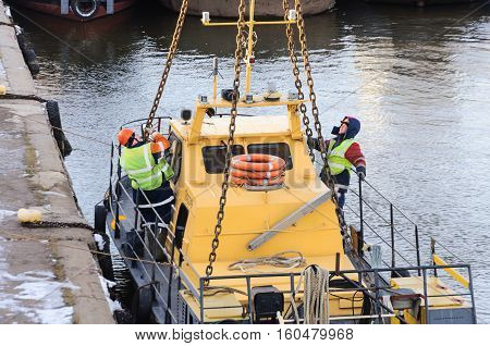 MOSCOW, RUSSIA - NOVEMBER 11, 2016: State Unitary Enterprise Mosvodostok performs recovery vessels on coastal winter parking. Several workers slingers hooked to the vehicle chain slings.