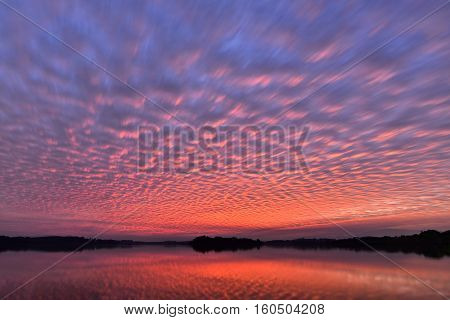 Beautiful sunset sky with colourful altocumulus clouds with reflexion over the lake natural background photo texture