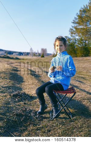 a girl sits on a stool on the meadow in summer