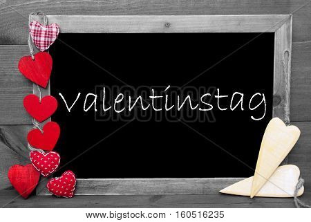 Chalkboard With German Text Valentinstag Means Valentines Day. Red Hearts. Wooden Background With Vintage, Rustic Or Retro Style. Black And White Image With Colored Hot Spots.