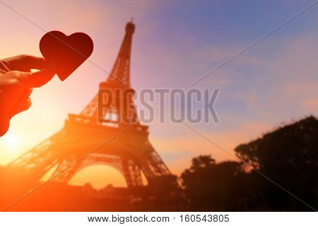 silhouette of romantic lovers hand hold love heart paper with eiffel tower in Paris with sunset