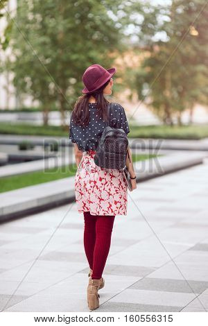 Asian student street style. Woman standing in full length outside with backpack and tablet pc in casual look against blurred city space. Beautiful young mixed race Asian Caucasian woman. Rear view.