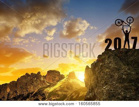 Silhouette of happy cyclist celebrating the New Year 2017 at sunset.