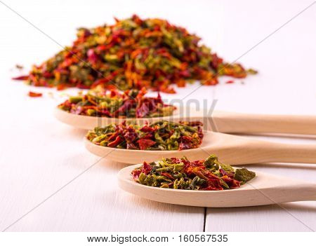 three wooden spoons with dried peppers and seeds (chili peppers habanero jalapeno rawit birds eye chili thai chili) on a white wooden place.