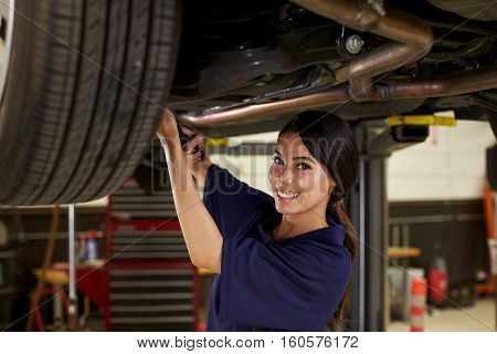 Portrait Of Female Auto Mechanic Working Underneath Car