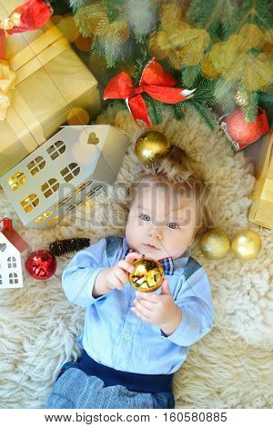 Cute Portrait Of Little Baby Celebrates Christmas. New Year's Holidays. Boy In Boytie Lies Under The