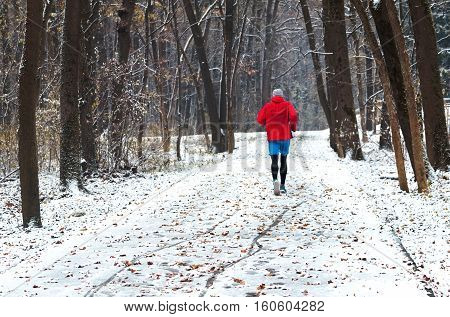 Athlete man runner running at winter time in city park or forest. Runner jogging in snow. Outdoor sport and fitness concept. Active lifestyle