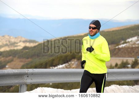 young healthy sport man running on asphalt road at snow mountains in trail runner hard workout in energy and endurance concept with a beautiful cold winter background