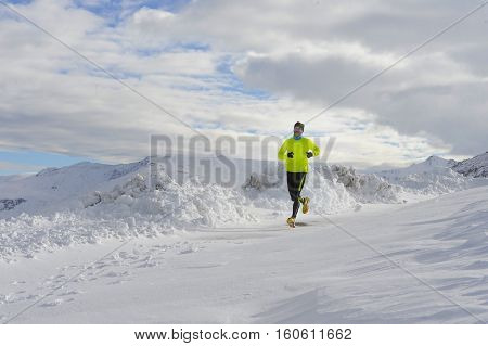 young healthy sport man running in snow mountains in trail runner hard workout in energy and endurance concept with a beautiful cold winter background
