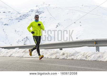 young healthy sport man running on asphalt road at snow mountains in trail runner hard workout in energy and endurance concept with a beautiful cold winter background