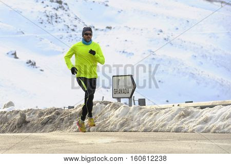 young healthy sport man running on asphalt road at snow mountains in trail runner hard workout in energy and endurance concept with a beautiful cold winter background
