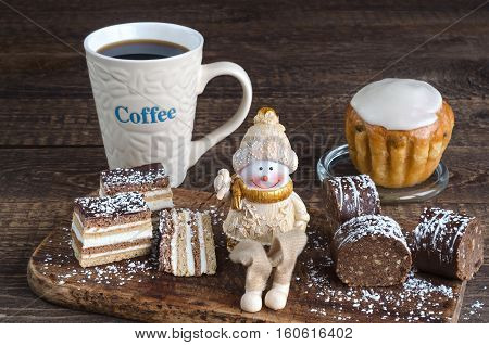 Variety of cakes dusted with powdered sugar, a toy Snowman and coffee mug with the inscription on the wooden surface.