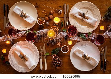 Christmas table setting for family dinner at a cosy rustic table with candles and decorations. Top view.