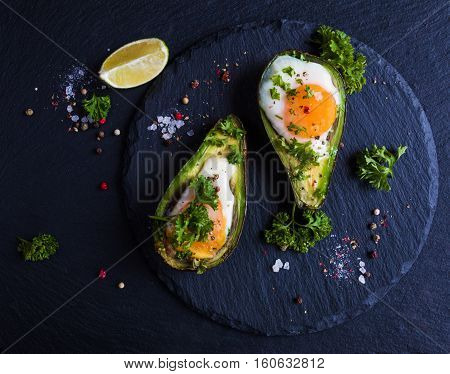 Avocado baked with eggs fresh parsley ground pepper. Black stone background top view.