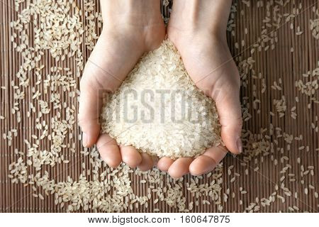 Female hands full of parboiled rice on bamboo mat background