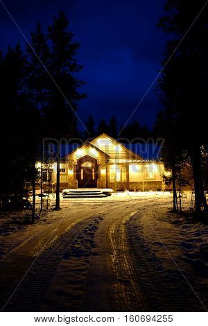 Cabin in stand of pine trees covered in snow in the winter in the evening with blue sky
