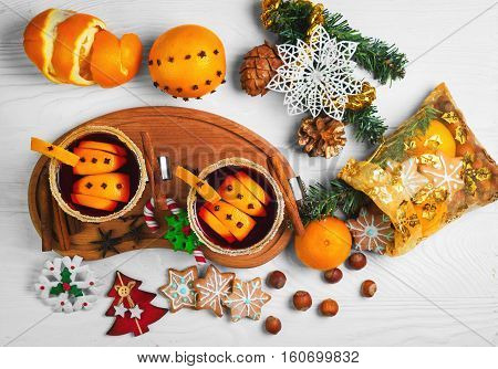 Winter Christmas drink hot mulled wine. Ingredients for mulled wine oranges cinnamon anise. Glasses with mulled wine decorated with sugar. Christmas gift with sweets nuts. White wooden background. Top view