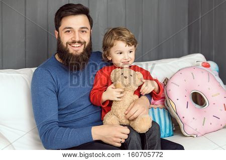 Happy family. Father and son with toy bear playing together at home on sofa