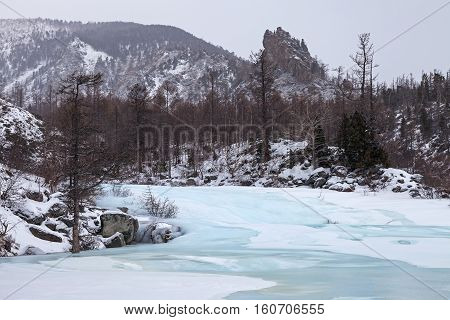 Winter mountain landscape with river covered with blue ice in soft colors