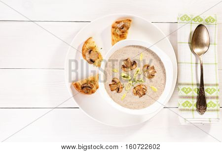 Soup with champignons leek and crispy croutons on white background top view.