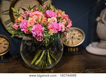 Bouquet of pink roses on a blue background wall with vintage clock in a round glass vase