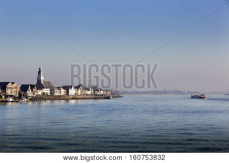 Village Lekkerkerk near the river Lek in the Netherlands. An industrial ship is passing by.