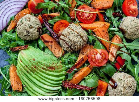 Vegan salad: avocado sweet potato lentil cutlets tomatoes arugula onions on black stone background with a copy space in the center