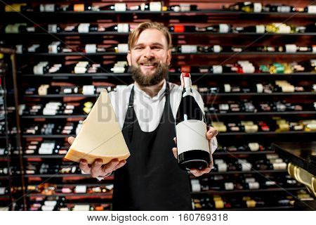 Portrait of a sommelier in uniform with parmegiano cheese and bottle of wine at the restaurant or supermarket. Choosing wine according to the type of cheese. Bottle with empty label to copy paste