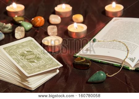 Moscow, Russia - December 4, 2016: Tarot card deck with book, green pendulum and candles. Esoteric background