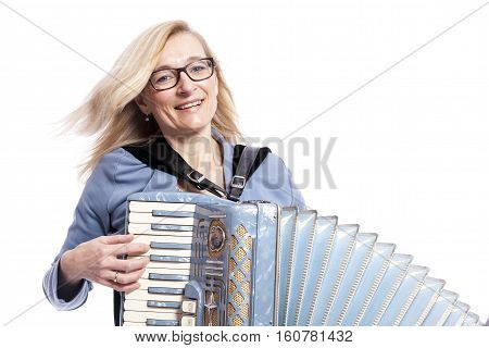 blond woman in blue with glasses plays the accordeon and smiles in studio with white background