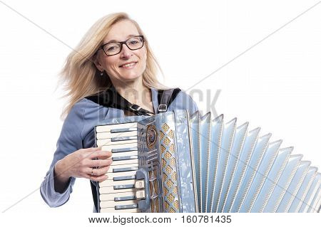 blond woman in blue with glasses plays the accordeon and smiles in studio with white background