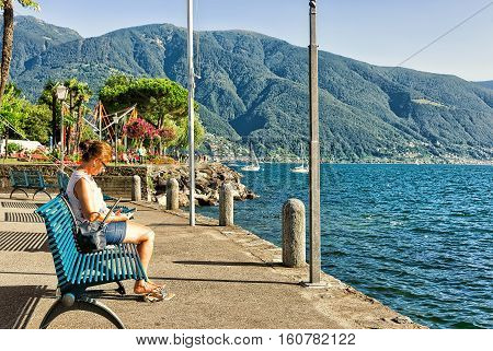 Ascona Switzerland - August 23 2016: Woman sitting on the bench at the embankment of the expensive resort in Ascona on Lake Maggiore Ticino canton Switzerland.