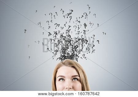 Close up of a blond woman's head with a swarm of question marks flying out of it. Gray background. Concept of tabula rasa