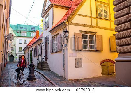 Riga, Latvia - September 22, 2016: Woman rides a bicycle near beautiful old buildings with window shutters in the old town of Riga