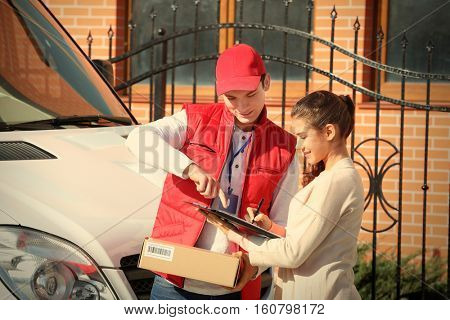 Young woman signing receipt for delivering parcel from male courier