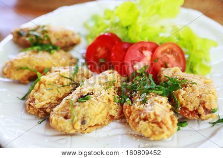 fried chicken wings or fried chicken with vegetable and sauce on white dish. fried chicken is bad cholesterol and bad for health when eating a lot. fast food for who work in city or office.