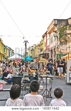 PHUKET THAILAND SEPTEMBER 27: Street artist musician entertains tourists at the walking street among old building Chino Portuguese style on street of Phuket town Thailand on September 27 2016.