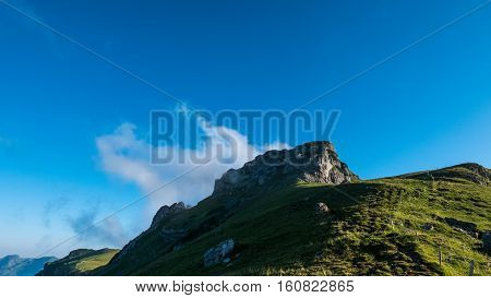 Clouds behind a mountain peak with a blue sky in the background