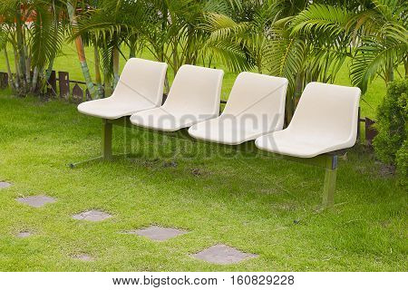 Four empty chairs oon lush green lawn with trees in a park.