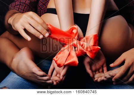 man holding female sexy buttocks of young woman with slim body and legs with bare back in lingerie has red ribbon bow on hands