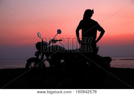Young man standing near motorbike and enjoying sunset view