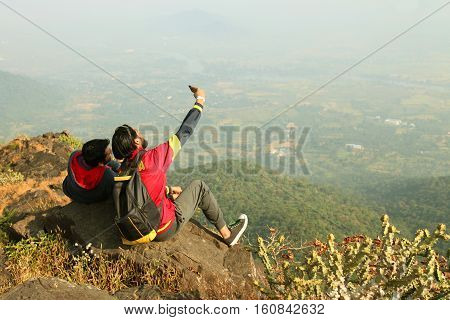 Two Young boys with backpack taking Selfie on the top of a mountain and enjoying valley view