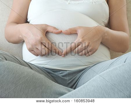 Pregnant woman holding her fingers in heart shape. Maternity concept and Baby Shower.